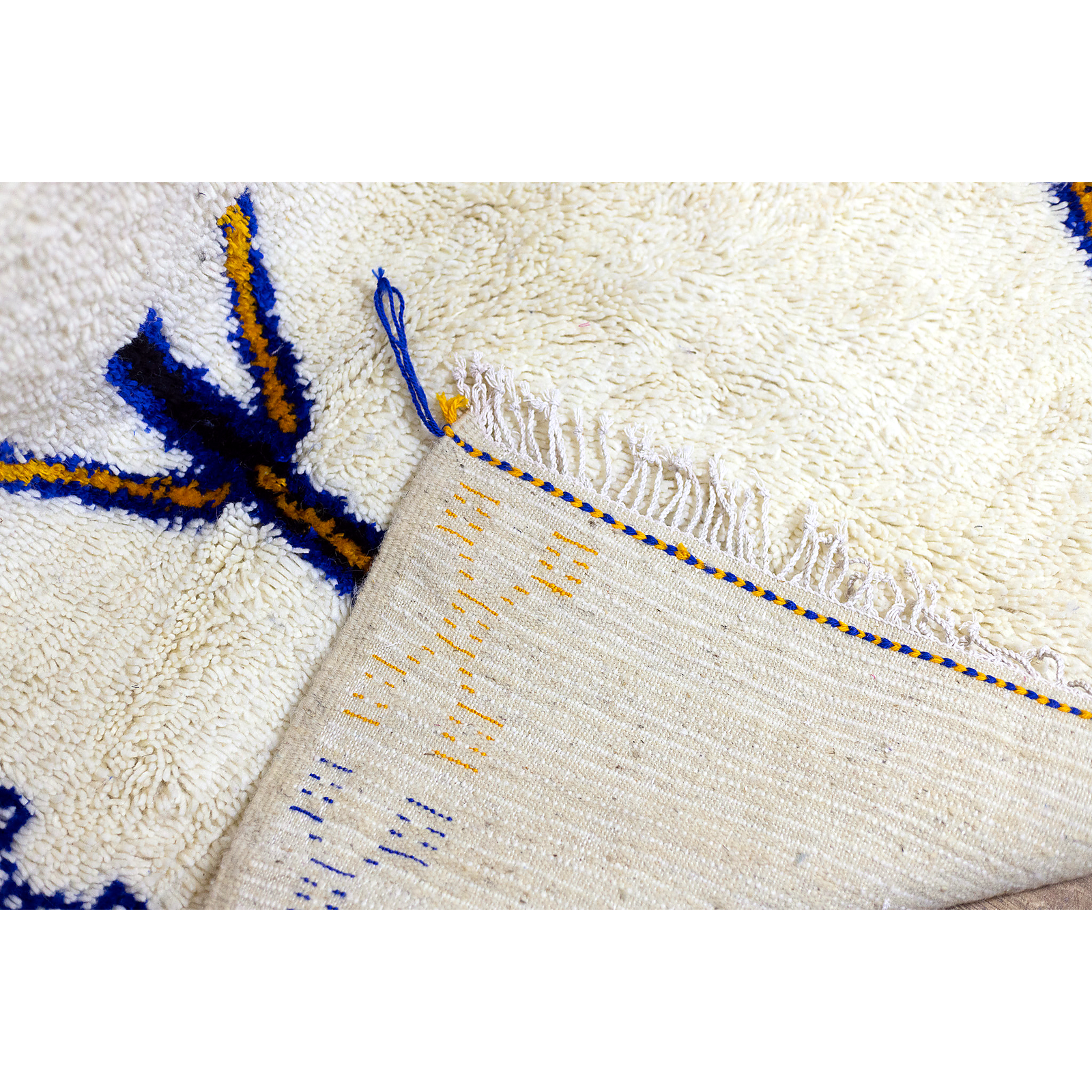 Border and motif detail of Moroccan Azilal rug with saffron and indigo symbols.