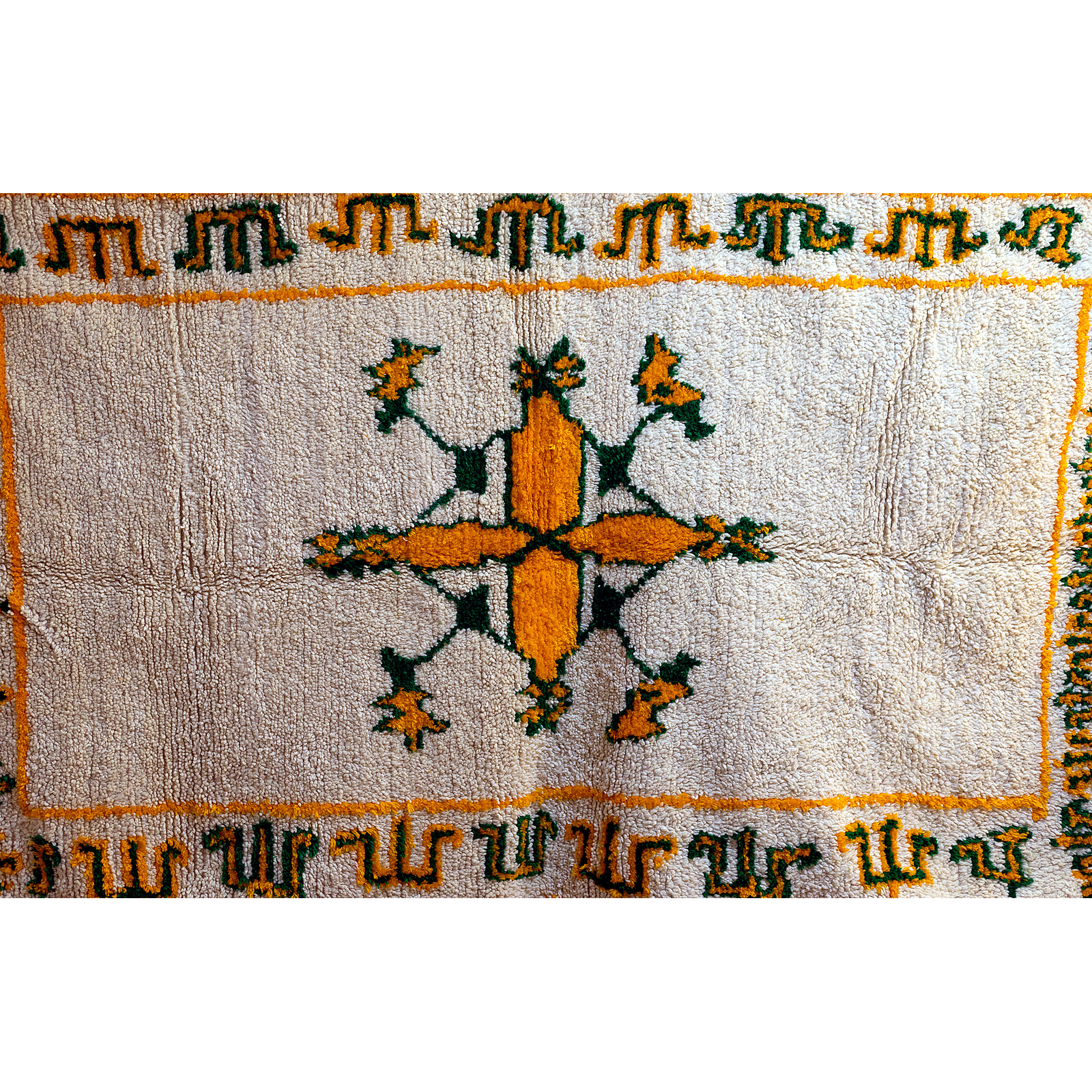 Border detail with green Amazigh designs on ivory Moroccan rug.